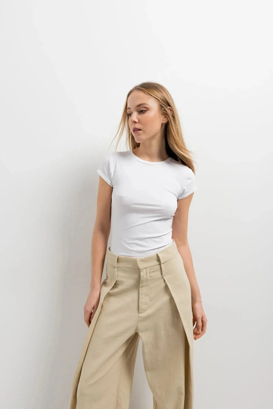 Femme portant un t-shirt blanc et un pantalon large et fluide femme beige dans une ambiance intimiste.