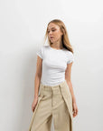 Femme portant un t-shirt blanc et un pantalon large et fluide femme beige dans une ambiance intimiste.