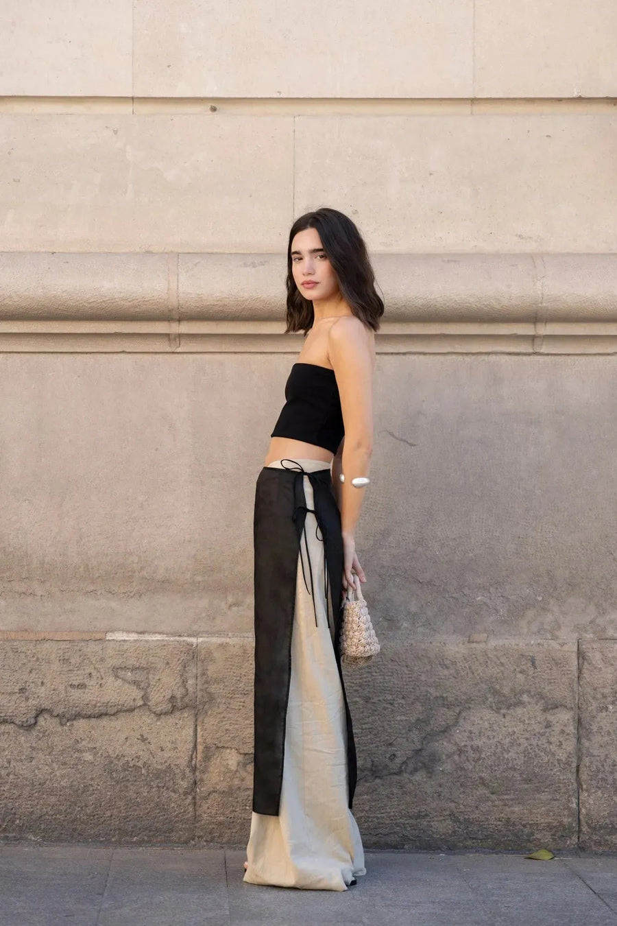 Femme en profil avec un pantalon large et fluide femme beige, top noir assorti, se tenant dans une rue moderne.