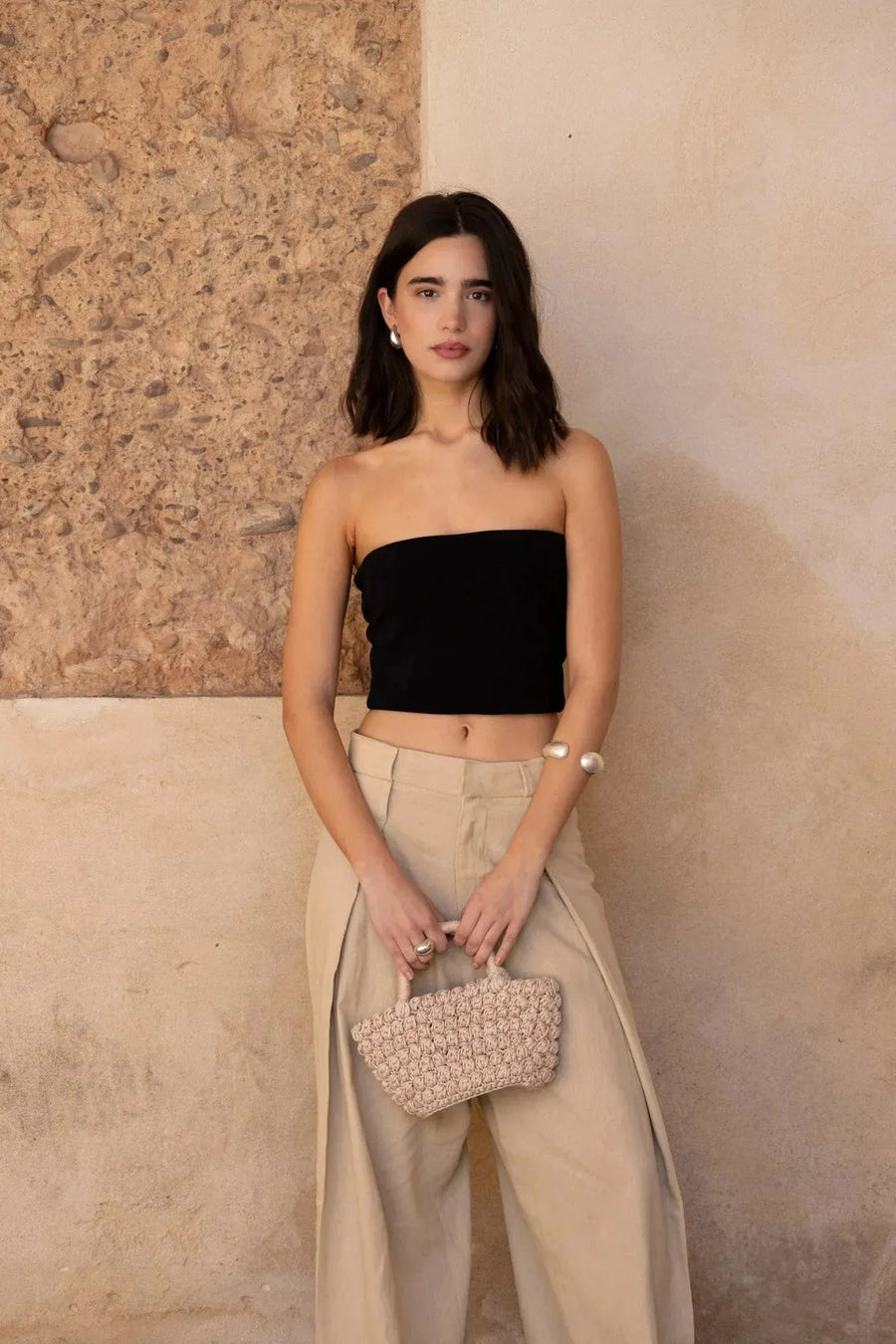 Femme portant un pantalon large et fluide beige en lin avec taille structurée et plis creux, style décontracté, blouse noire, dans un décor naturel.