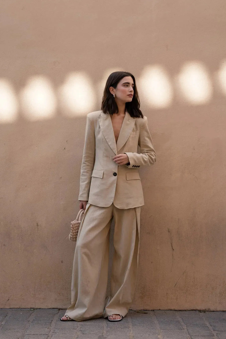 Femme portant un costume beige, associe un pantalon large et fluide femme avec un blazer chic dans un cadre minimaliste.