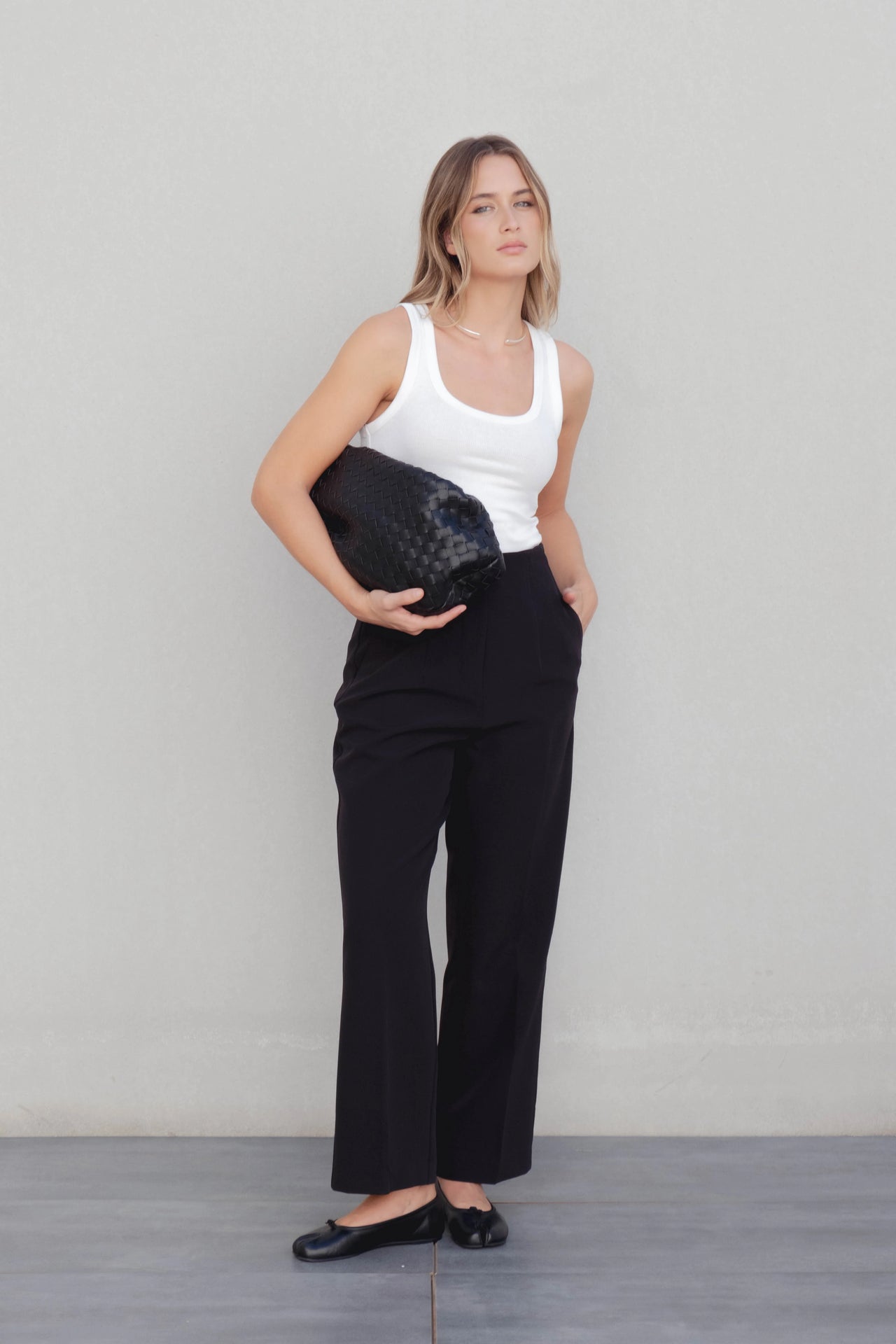 Femme posant avec un pantalon à pince femme noir et un sac élégant, combinant confort et style moderne.