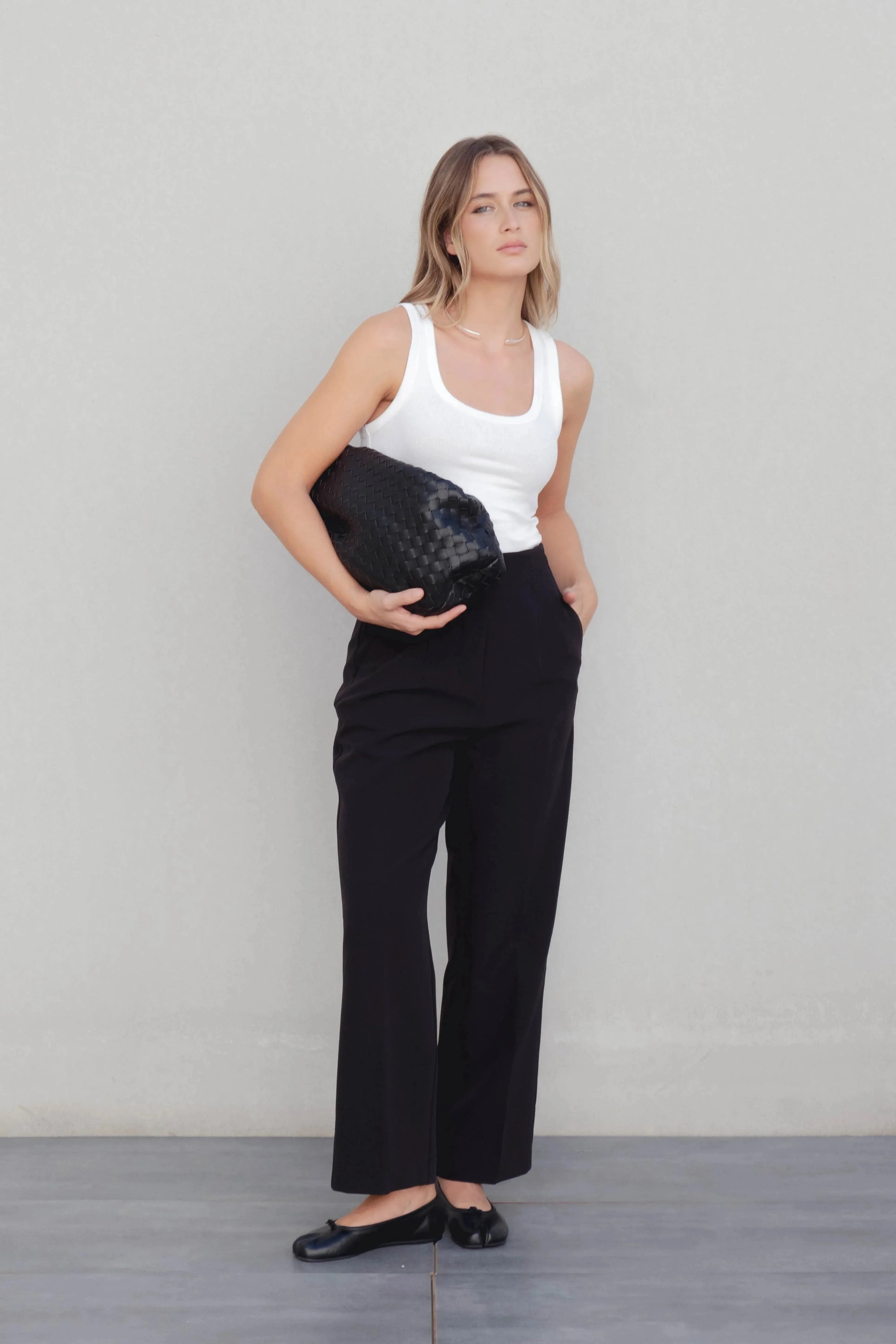 Femme posant avec un pantalon à pince femme noir et un sac élégant, combinant confort et style moderne.