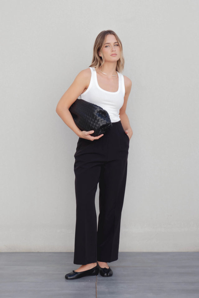 Femme posant avec un pantalon à pince femme noir et un sac élégant, combinant confort et style moderne.