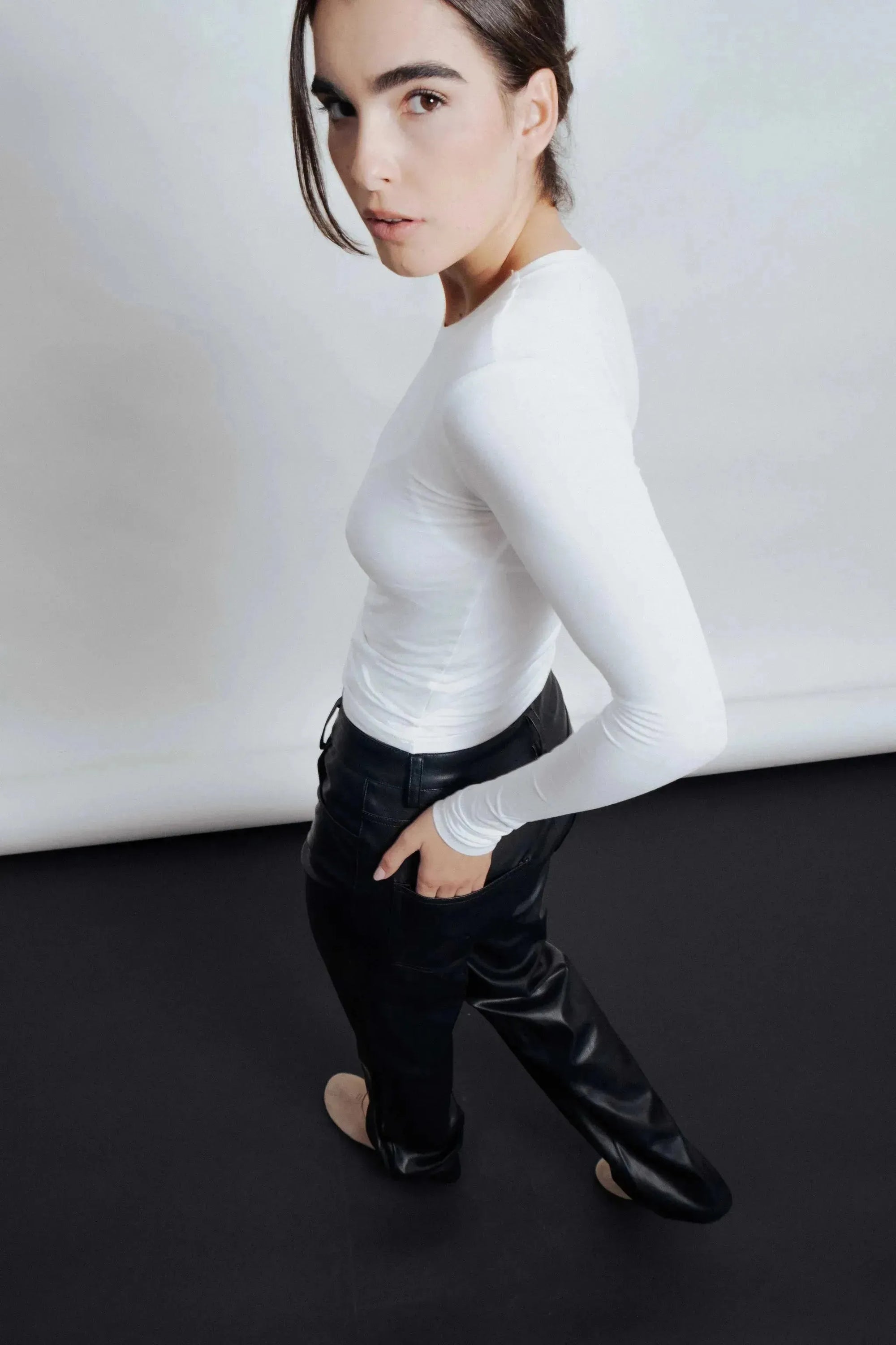 Une femme debout, vue de côté, mettant en valeur le pantalon imitation cuir femme, élégamment combiné avec un t-shirt blanc.