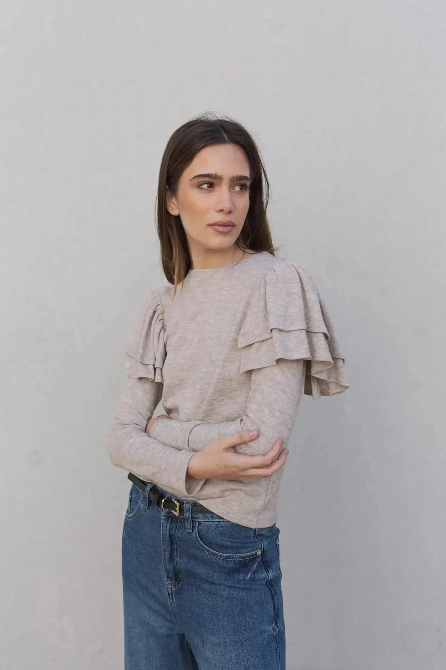 Gros plan sur une femme en pull à volants beige clair, mettant en avant les détails délicats. Ce pull maille fine femme est parfait pour allier confort et élégance.