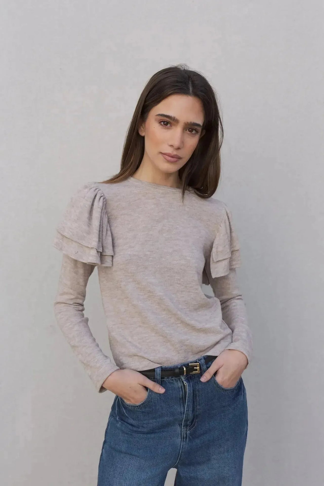 Portrait d'une femme dans un pull à volants beige clair, soulignant son élégance naturelle. Ce modèle de pull maille fine femme est un incontournable de la garde-robe.