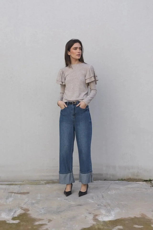 Une femme portant un pull à volants beige clair accompagné d'un jean tendance. Ce modèle de pull maille fine femme apporte élégance et confort pour toutes les occasions.