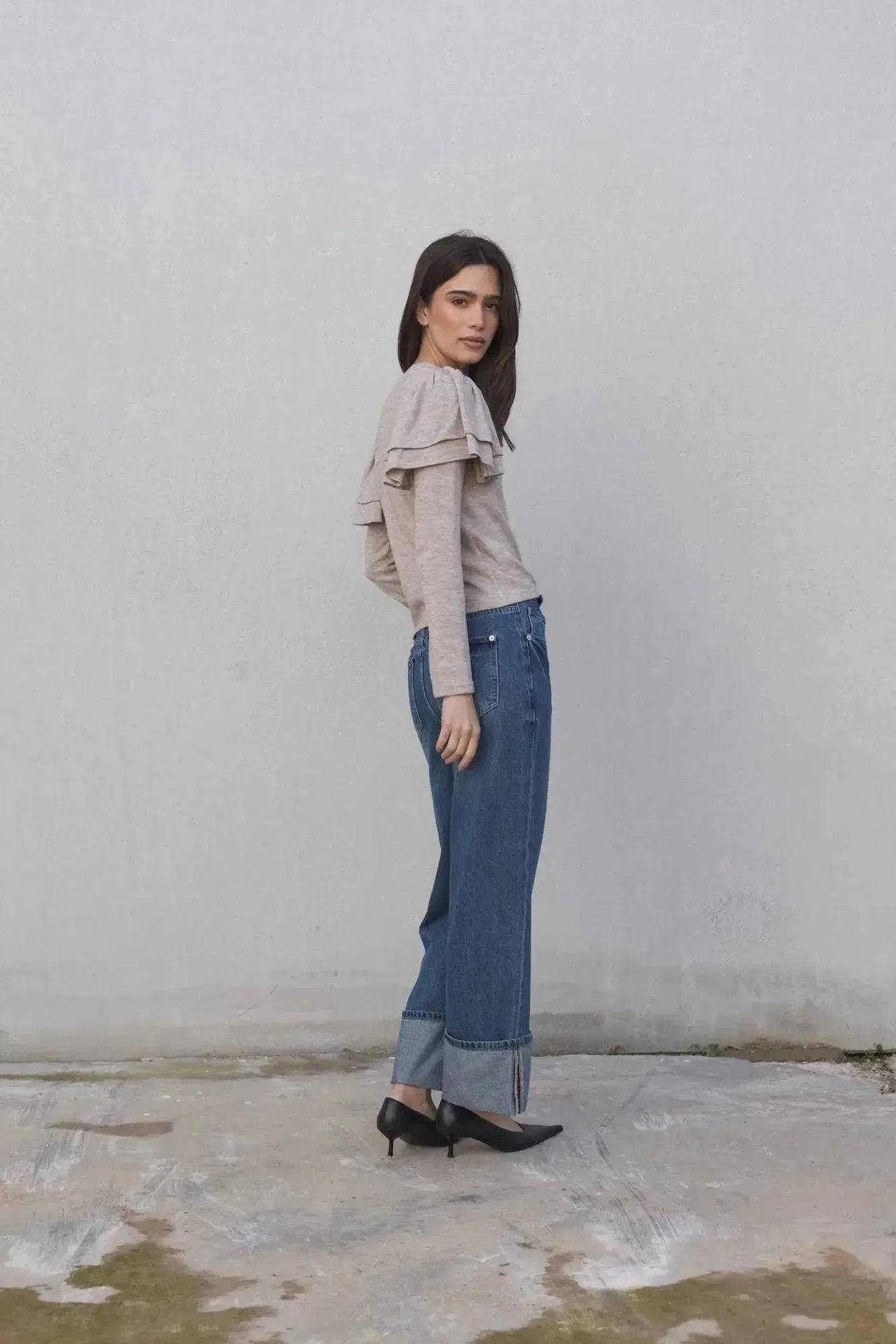 Femme vue de profil en pull à volants beige clair avec jeans décontractés. Le pull maille fine femme se distingue par son style raffiné et moderne.
