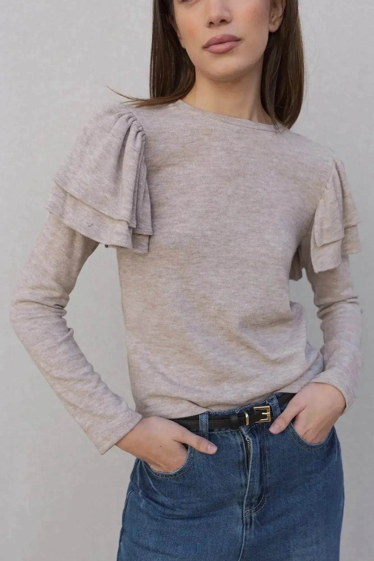 Une femme souriante portant un pull à volants beige clair, associé à un jean élégant. Ce pull maille fine femme est idéal pour une sortie décontractée ou chic.