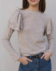 Une femme souriante portant un pull à volants beige clair, associé à un jean élégant. Ce pull maille fine femme est idéal pour une sortie décontractée ou chic.