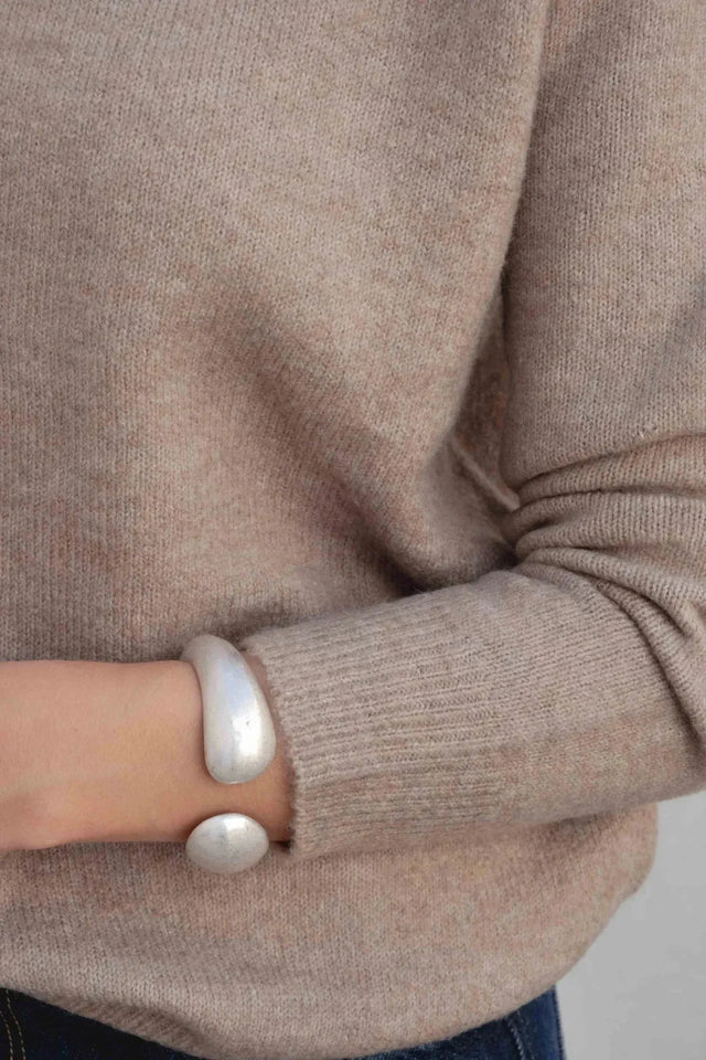 Détail du pull laine femme col rond marron avec un bracelet argenté, combinaison de style.