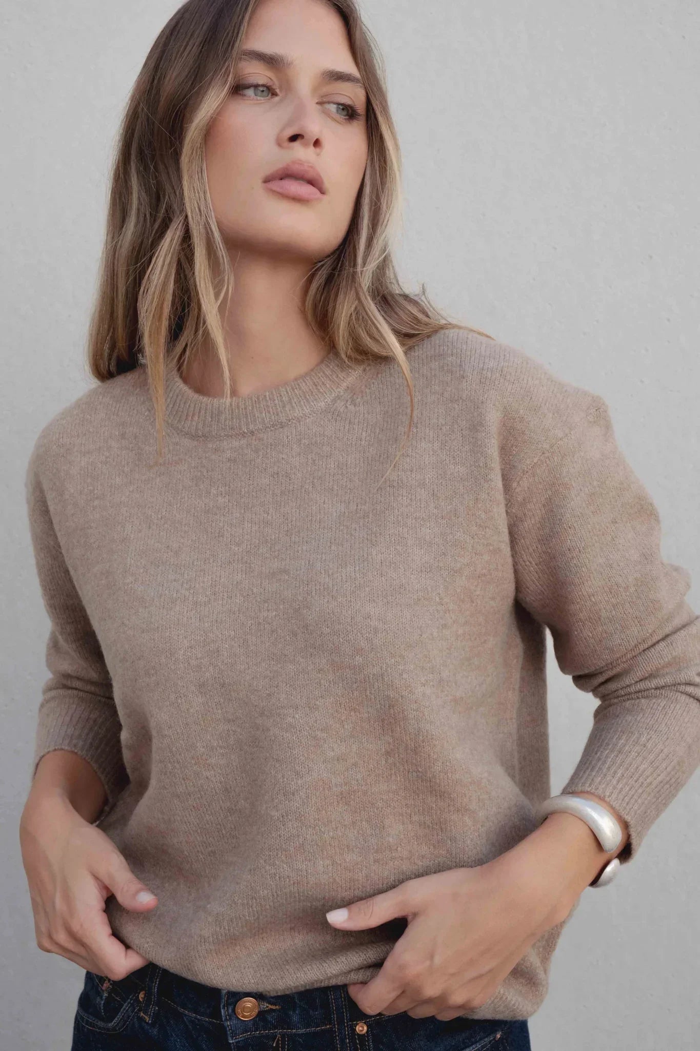 Femme portant un pull basique col rond en laine marron clair et jeans bleus foncés