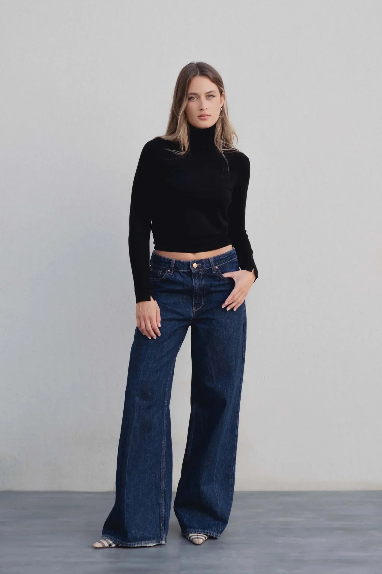 Femme debout avec un pull col roulé noir femme, associé à un jean large pour une tenue décontractée et stylée.