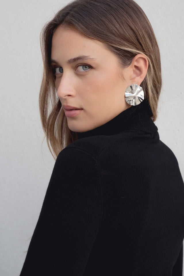 Femme avec un pull col roulé noir en maille fine, accessoirisée avec de grandes boucles d'oreilles, pour un look élégant.