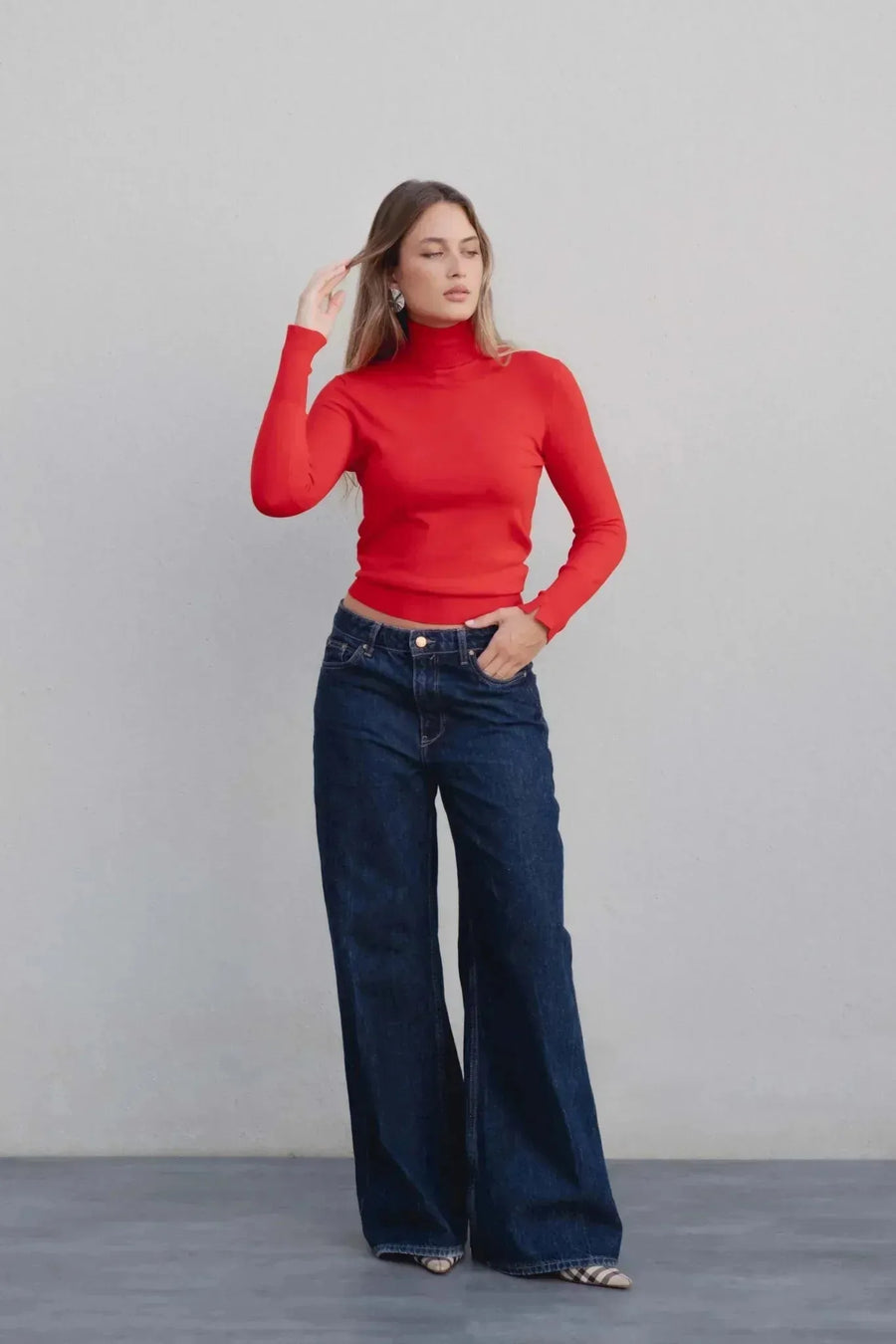 Modèle féminin posant en pull col roulé femme rouge avec jeans larges, capturant un style casual chic.