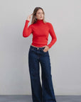 Modèle féminin posant en pull col roulé femme rouge avec jeans larges, capturant un style casual chic.