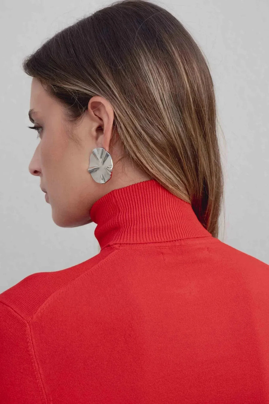 Vue arrière d'un modèle portant un pull col roulé femme rouge, soulignant le col stylé et les boucles d'oreilles modernes.