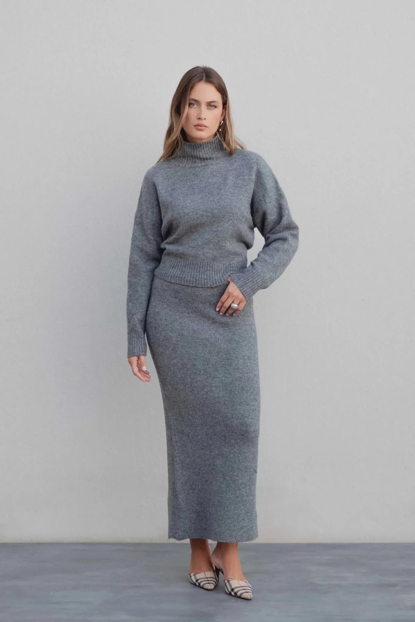 Pull court gris à col montant porté par une femme avec jupe midi assortie