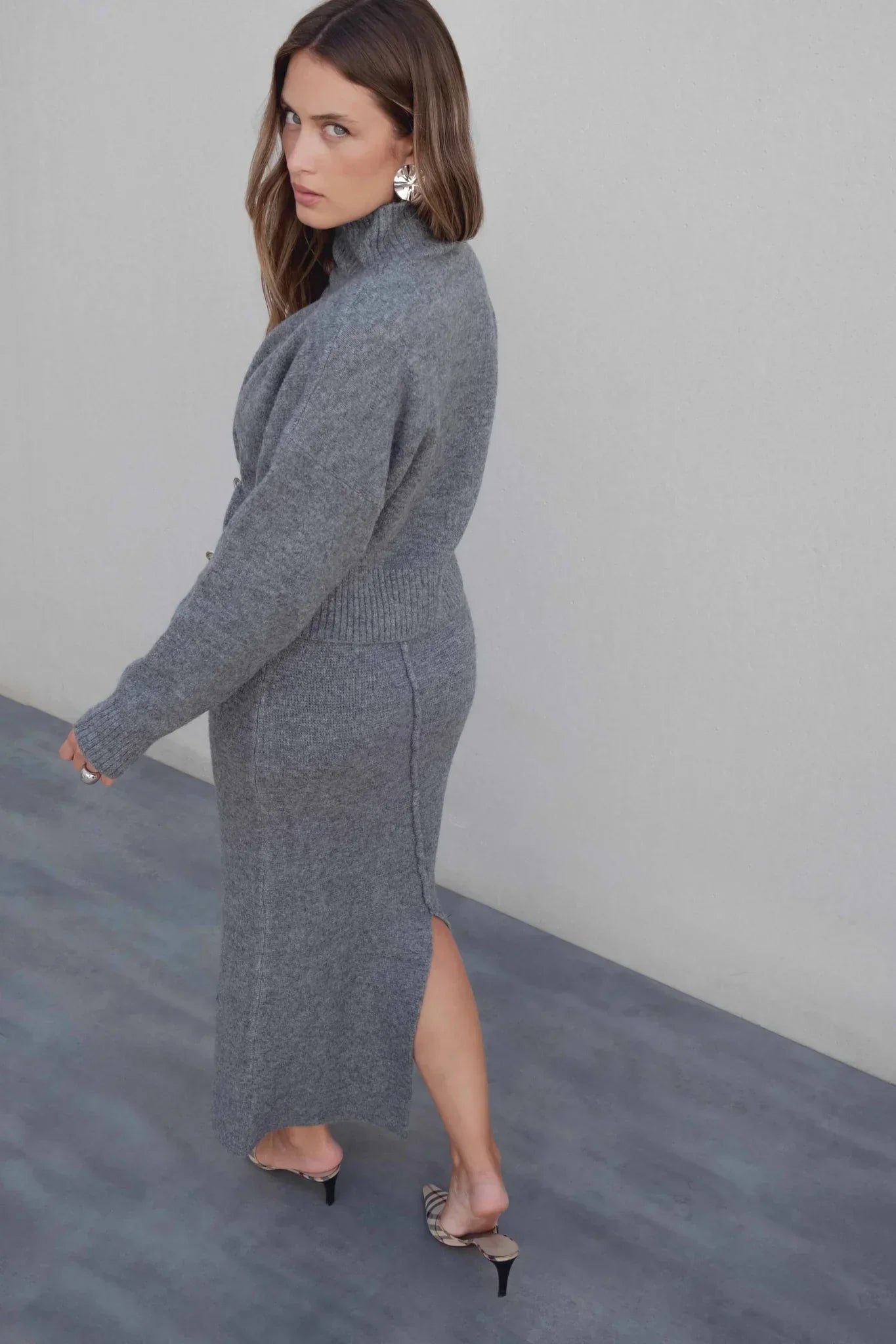Femme portant un pull court gris à col montant, jupe longue à fente et mules à motifs