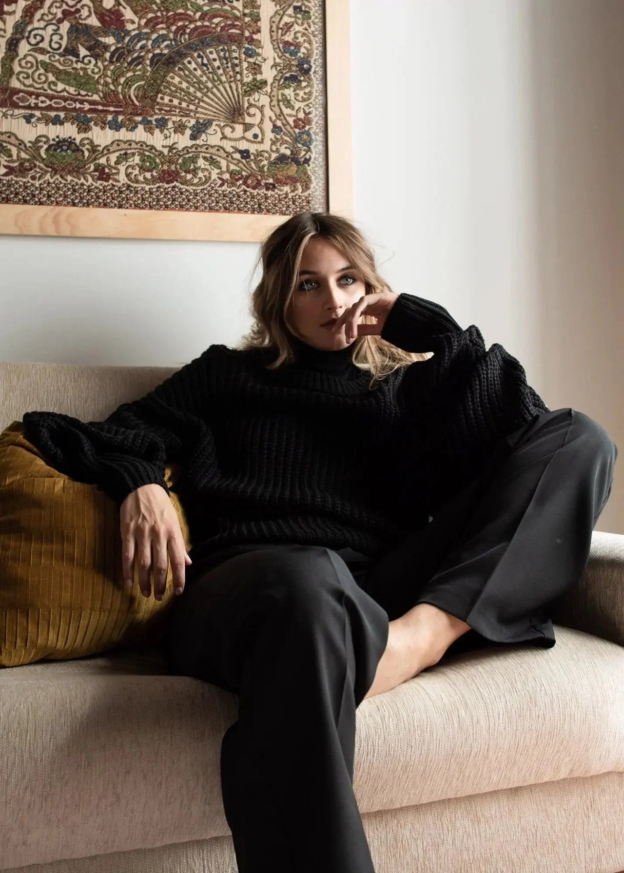 Pull Laine Femme Oversize à Manches Ballon - Femme détendue avec un pull laine femme noir, assise sur un canapé.