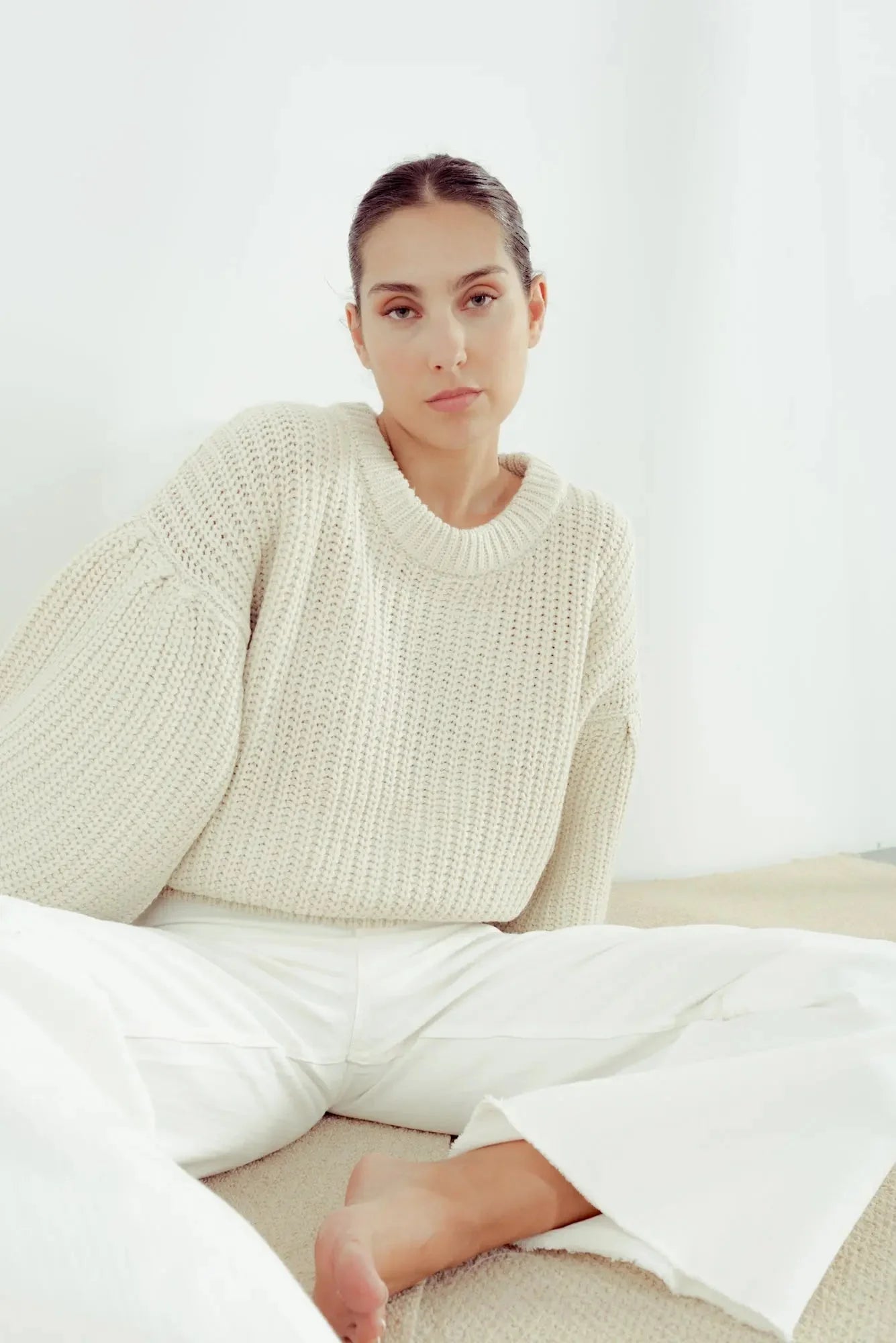 Femme portant un pull crème en tricot surdimensionné manches ballon et pantalon blanc