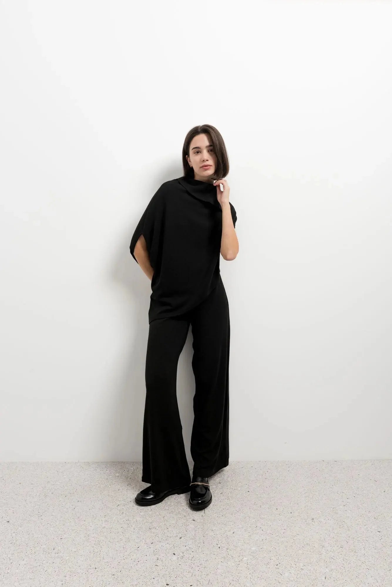 Femme portant un pull effet cap noir à col bénitier et pantalons larges, vêtements d’hiver