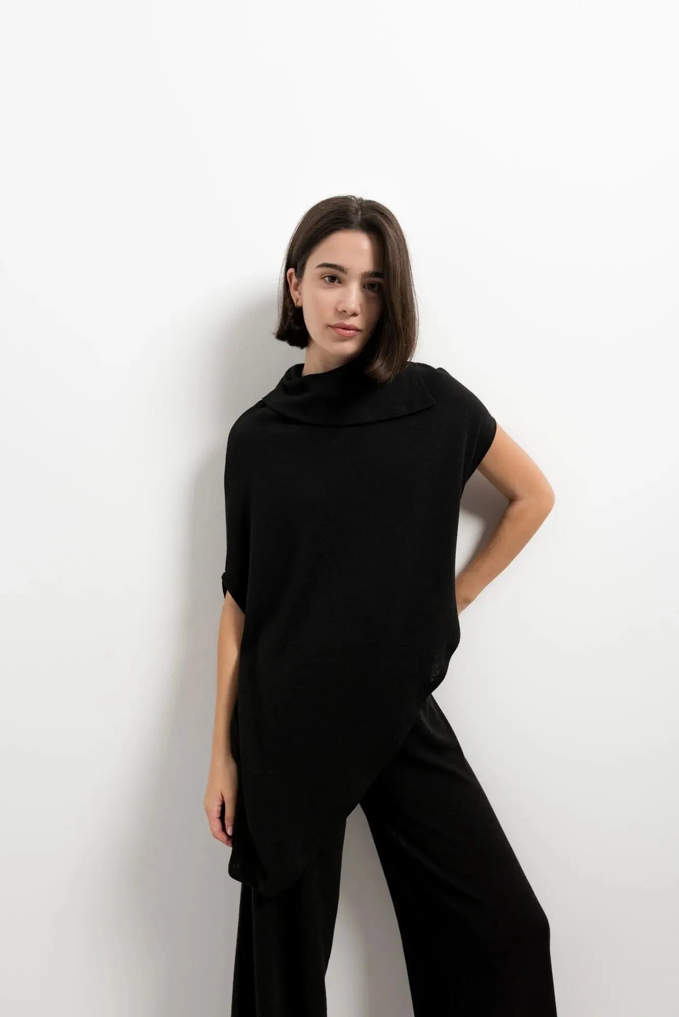 Femme portant un pull effet cap noir à col bénitier avec pantalon large