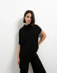 Femme posant en pull long femme noir à col bénitier, une pièce essentielle pour la saison hivernale.