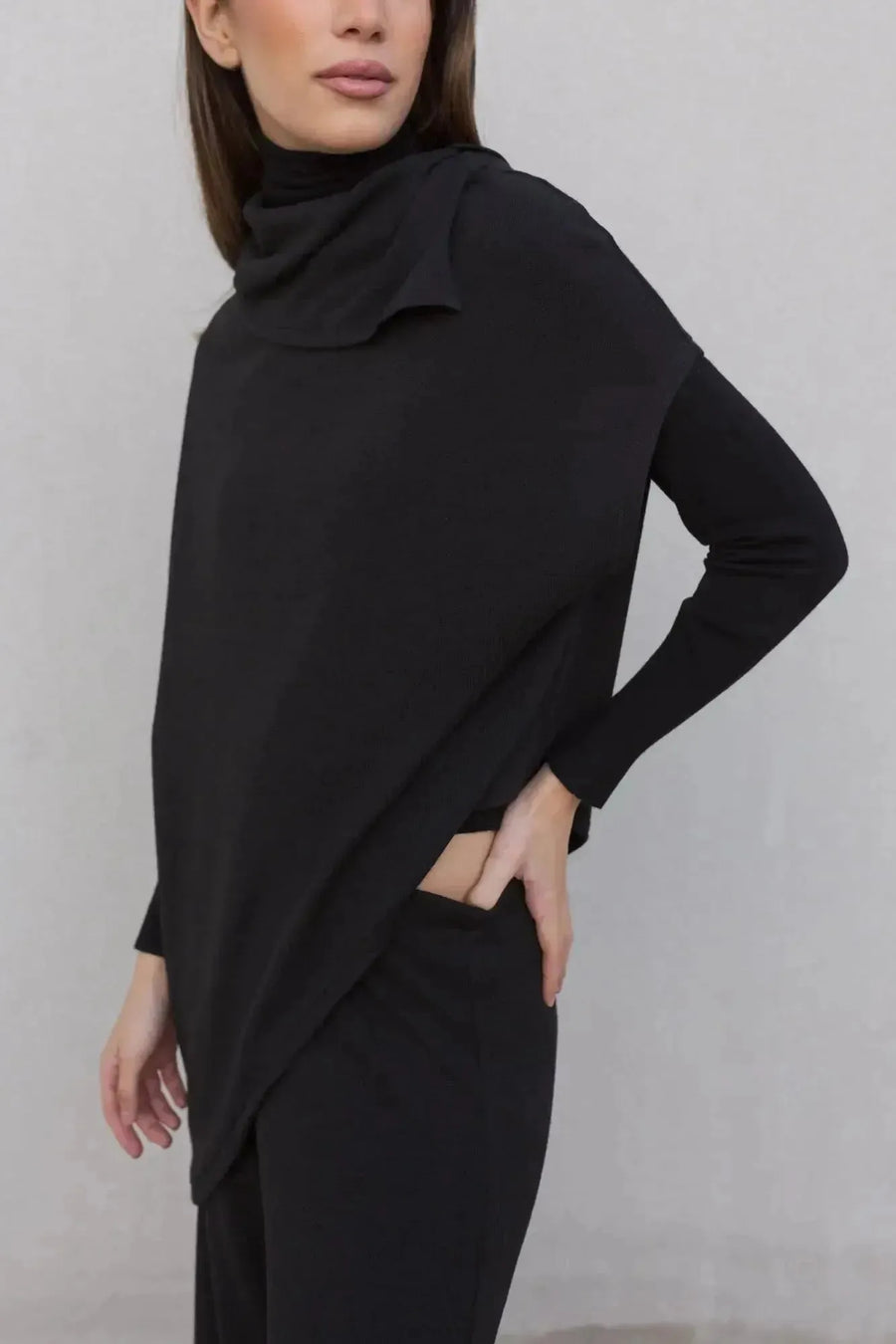 Femme portant un pull long femme noir à col bénitier, alliant élégance et confort pour l'hiver.