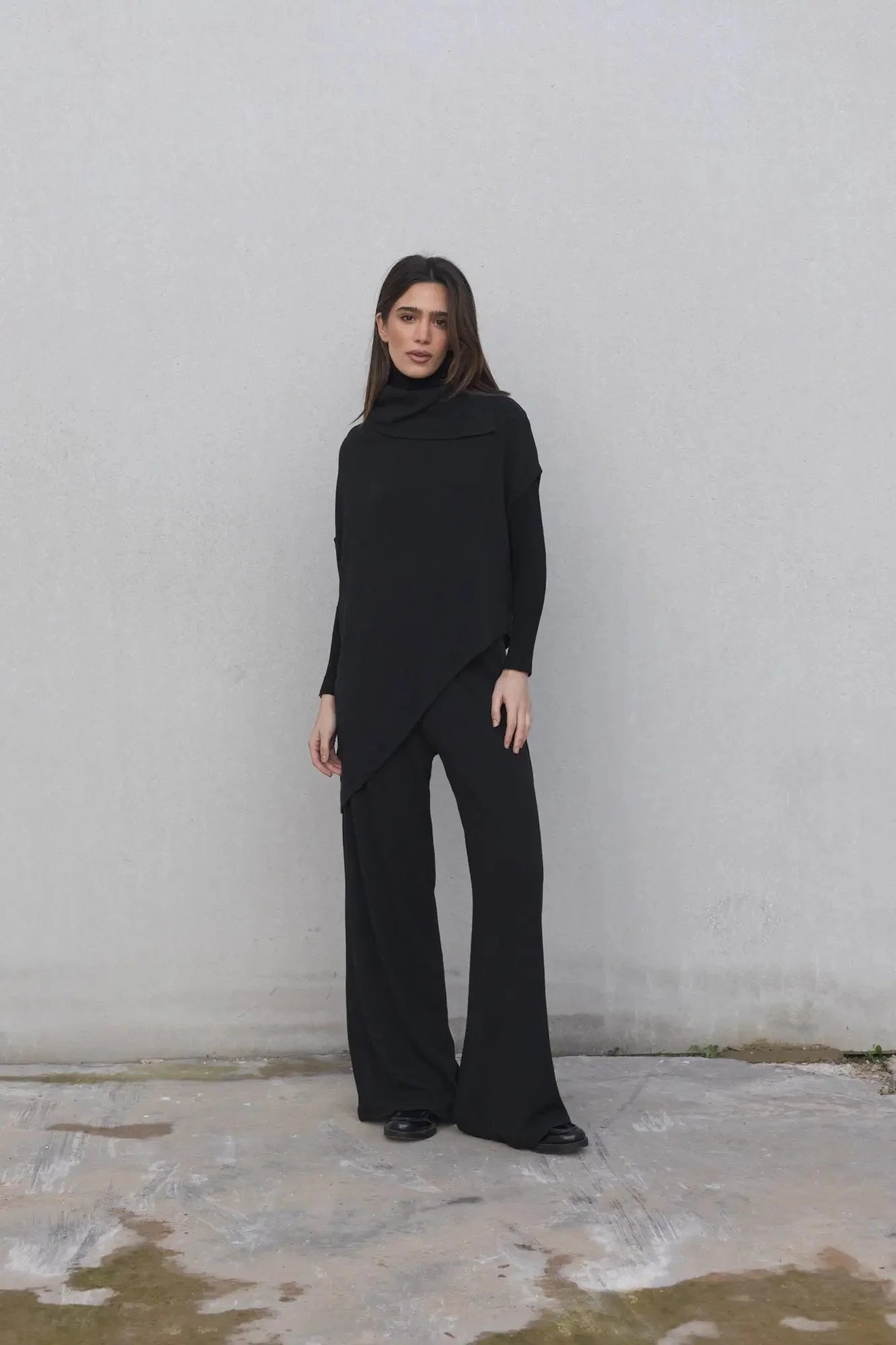 Femme portant un pull effet cap noir à col bénitier et pantalons larges, vêtements d’hiver
