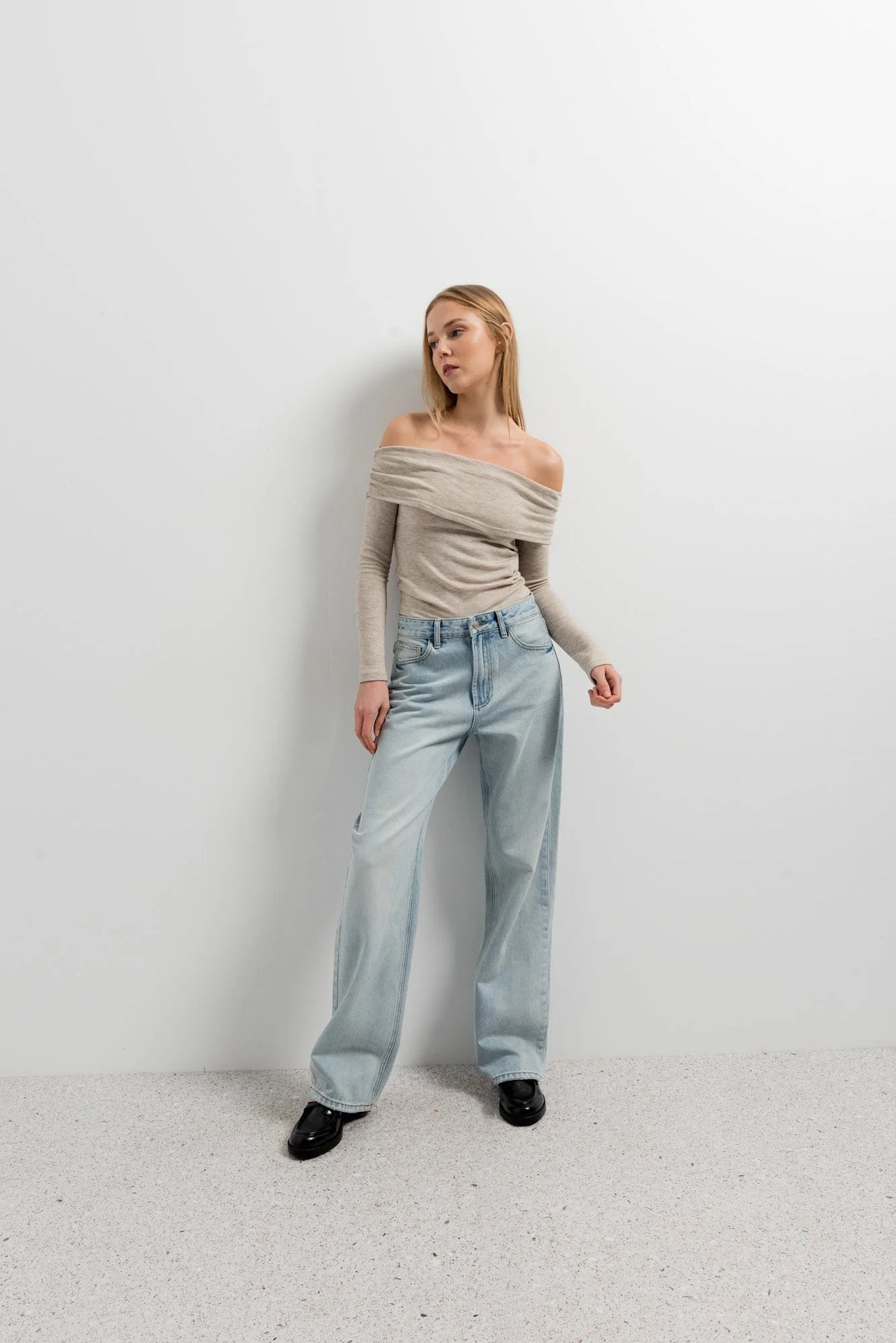 Modèle féminin affichant un pull épaule dénudée beige en tricot, stylisé avec un jeans, idéal pour une sortie décontractée.