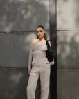 Femme posant avec un pull épaule dénudée beige en tricot, associé à un pantalon clair, capturant un style chic et sophistiqué.
