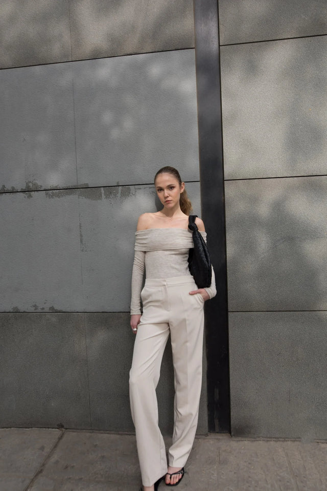 Model avec un pull épaule dénudée beige en tricot, porté avec un pantalon beige, illustrant une mode contemporaine et élégante.