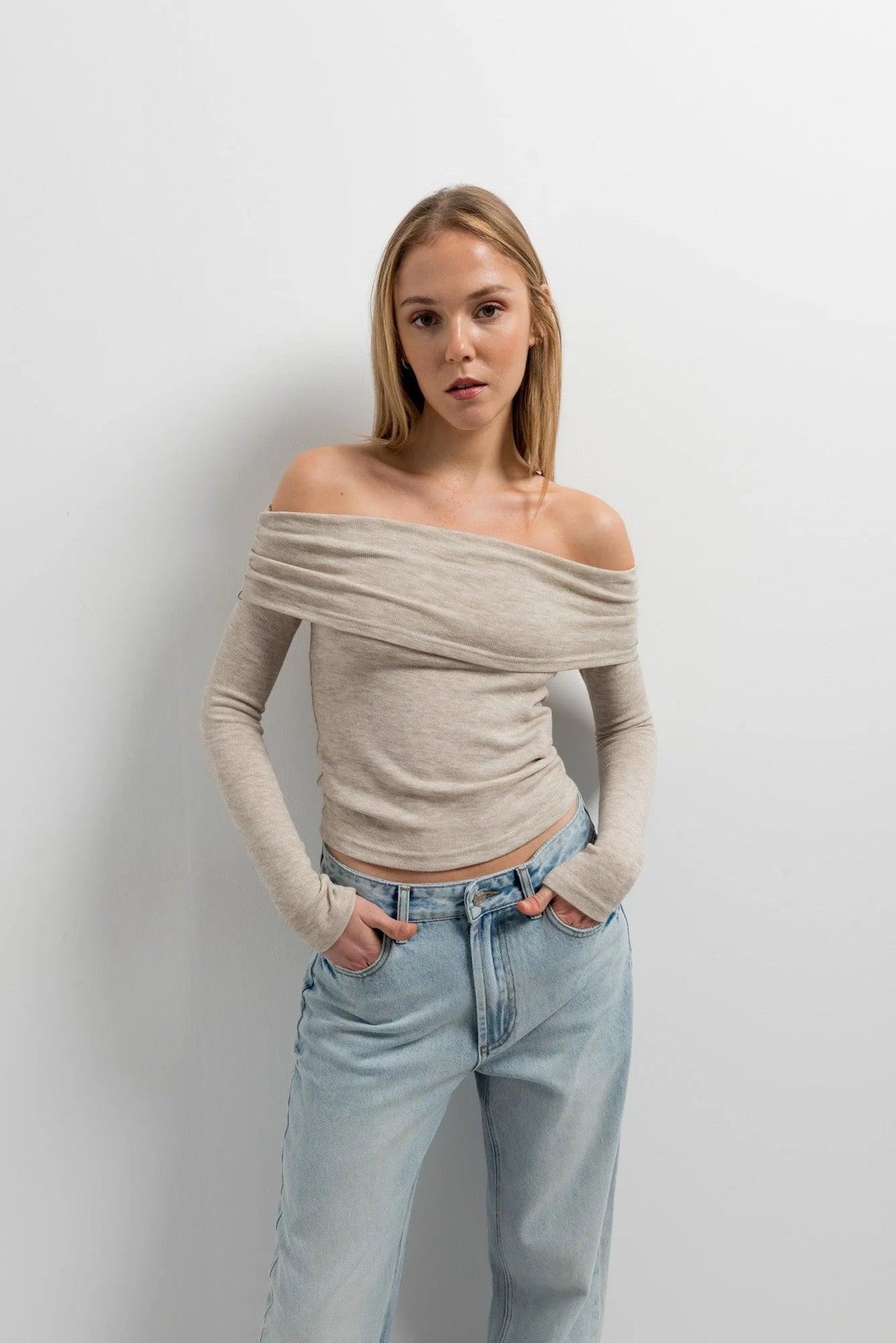 Femme dans un pull épaule dénudée beige en tricot, ajoutant une touche d'élégance à sa garde-robe tout en restant confortable.