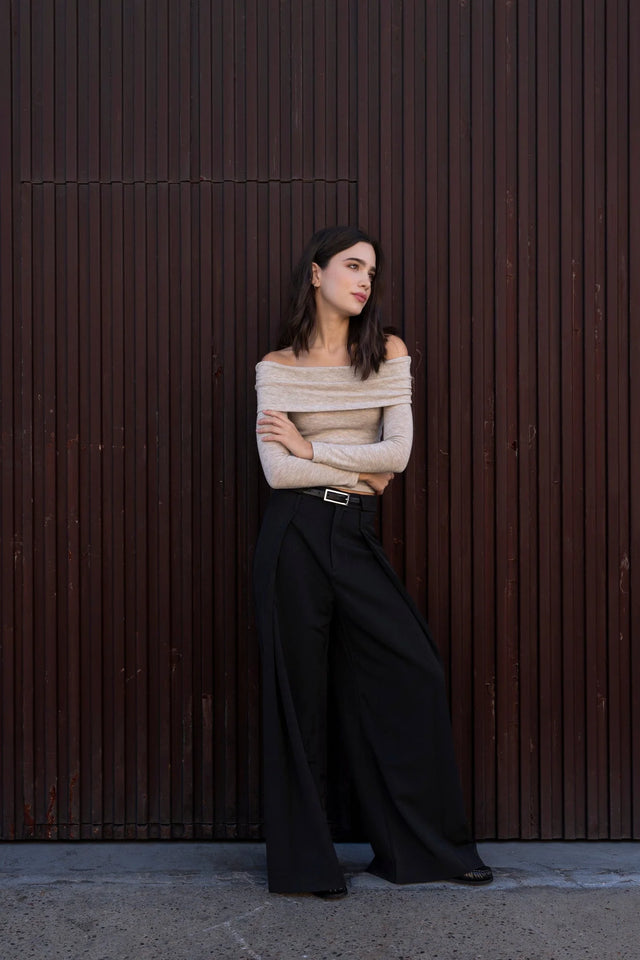 Femme élégante portant un pull épaule dénudée beige en tricot, regardant à distance, parfaite pour un look stylé.