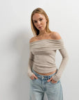 Femme portant un pull épaule dénudée beige en tricot, avec un look décontracté et moderne, parfait pour un style quotidien.