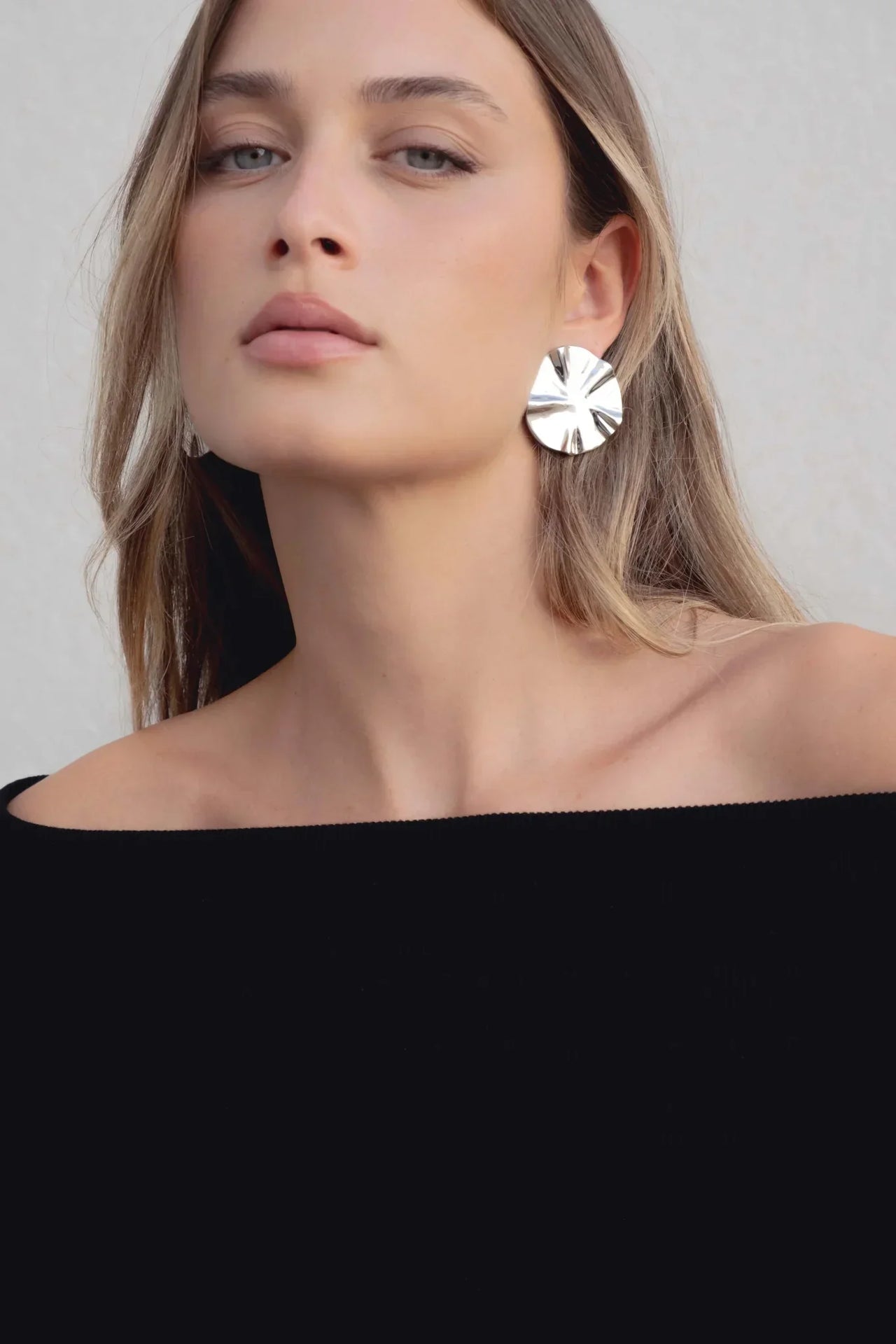 Gros plan sur le visage d'une femme portant un pull femme maille noir à épaules dénudées et des boucles d'oreilles brillantes.