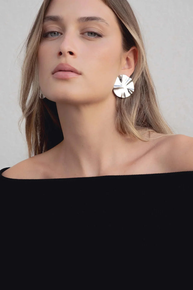 Gros plan sur le visage d'une femme portant un pull femme maille noir à épaules dénudées et des boucles d'oreilles brillantes.