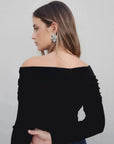 Femme vue de profil portant un pull femme maille noir à épaules dénudées, mettant en valeur son cou et ses boucles d'oreilles.