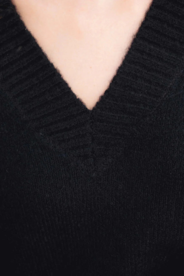 Gros plan sur le col V d'un pull oversize noir, mettant en avant la texture et le style intemporel, essentiel du pull laine femme.