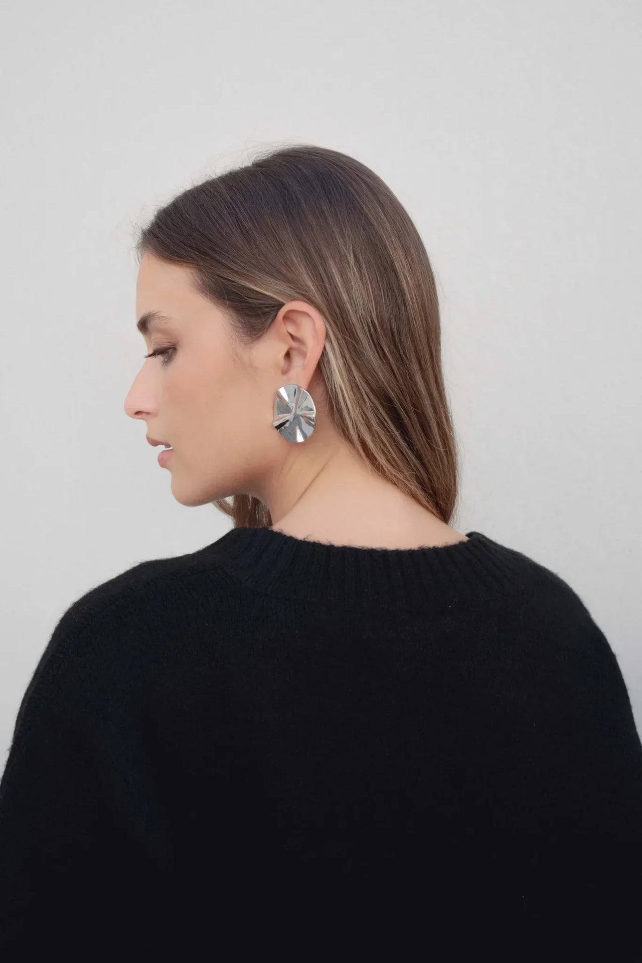Profil d'une femme portant un pull oversize noir col V, accent sur des boucles d'oreilles, parfait pour compléter un look avec pull laine femme.