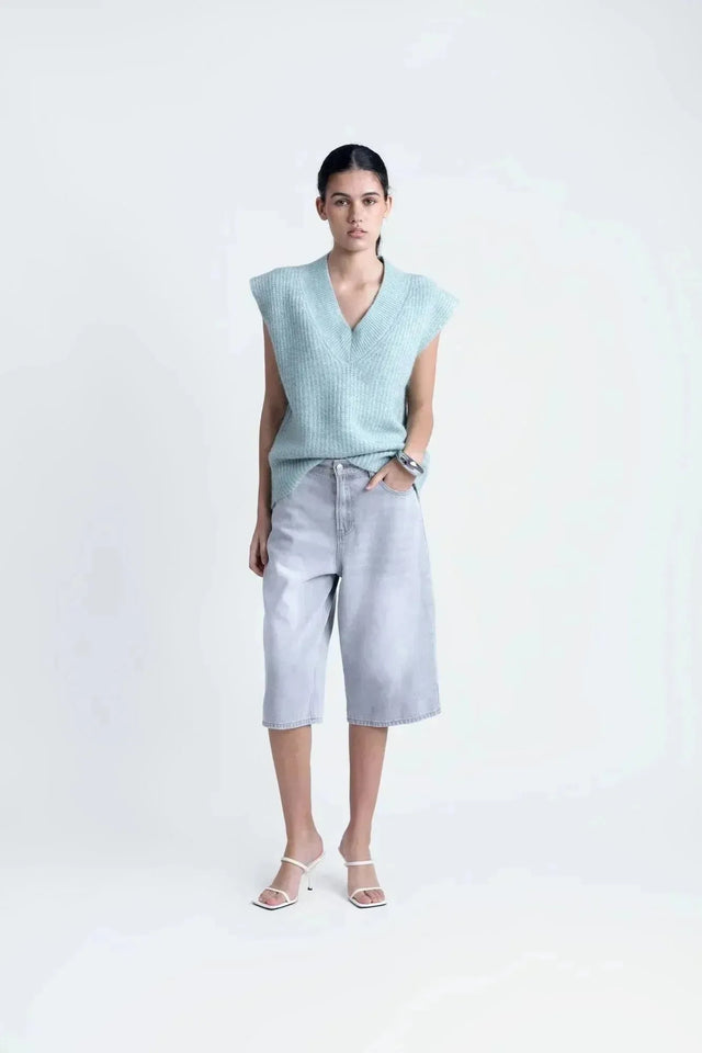 Modèle portant un pull sans manche femme oversize en tricot col V doux, combiné avec un short en jean, offrant un look élégant et décontracté.