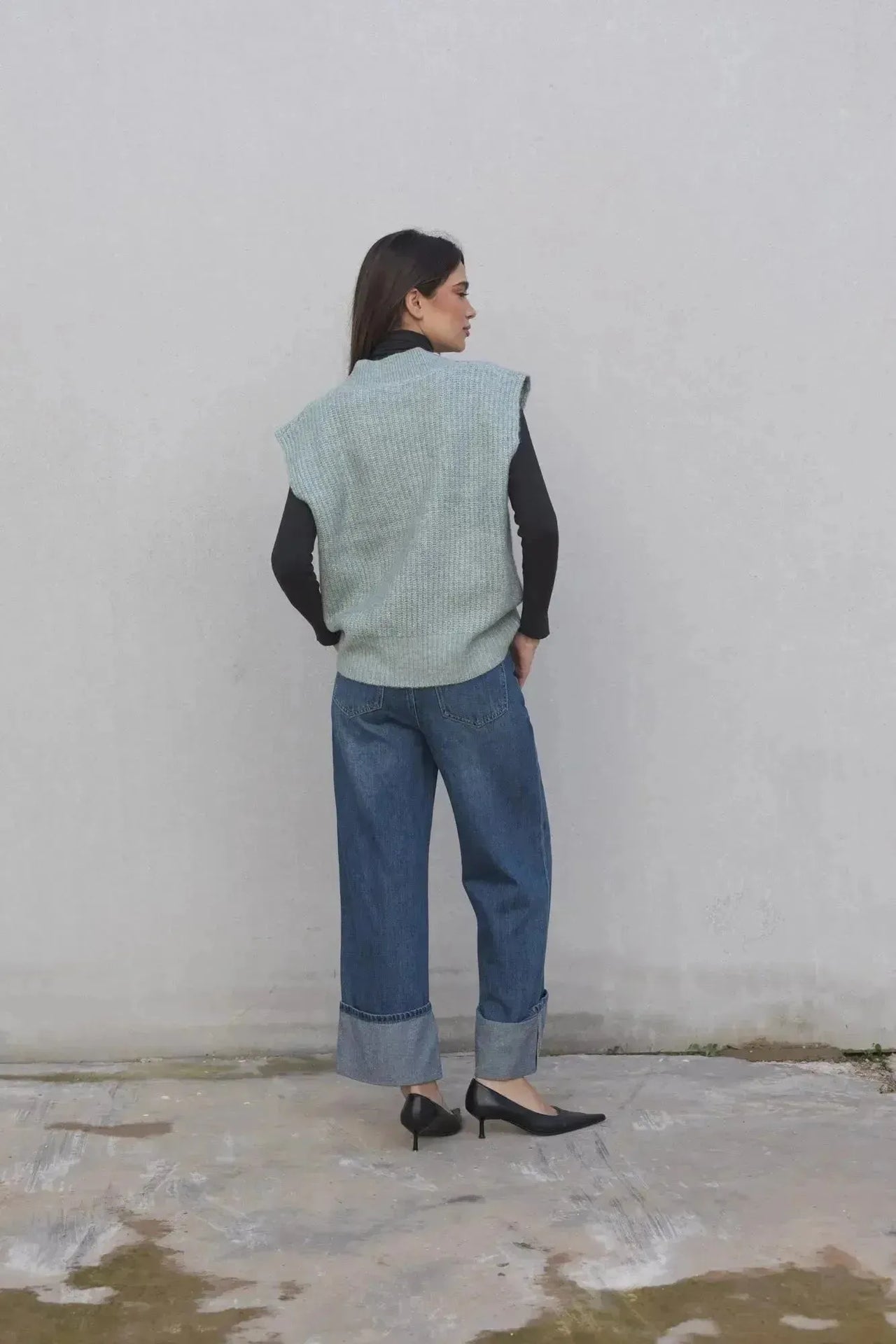 Femme avec un pull sans manche femme oversize en tricot col V doux, vêtue d'un jean, capturant un style à la fois chic et décontracté.
