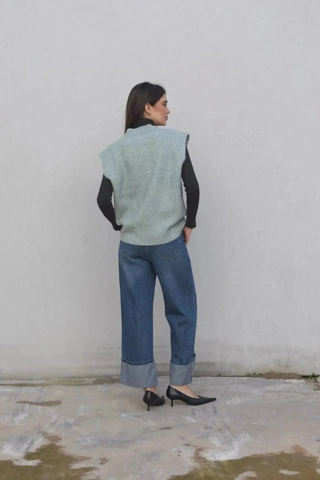 Femme avec un pull sans manche femme oversize en tricot col V doux, vêtue d'un jean, capturant un style à la fois chic et décontracté.