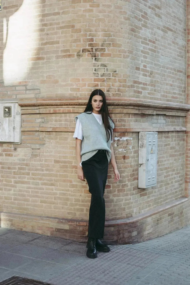 Femme debout avec un pull sans manche femme oversize en tricot col V doux, contrasté avec un pantalon noir, idéal pour un look urbain.