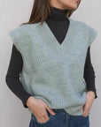 Femme élégante portant un pull sans manche femme oversize en tricot col V doux sur un col roulé, soulignant le confort et le style.