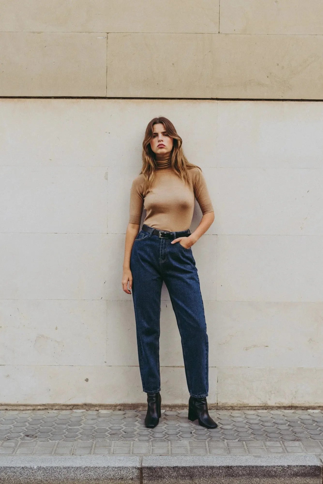 Femme portant un pull tricoté beige à col roulé, jeans foncés et bottines noires