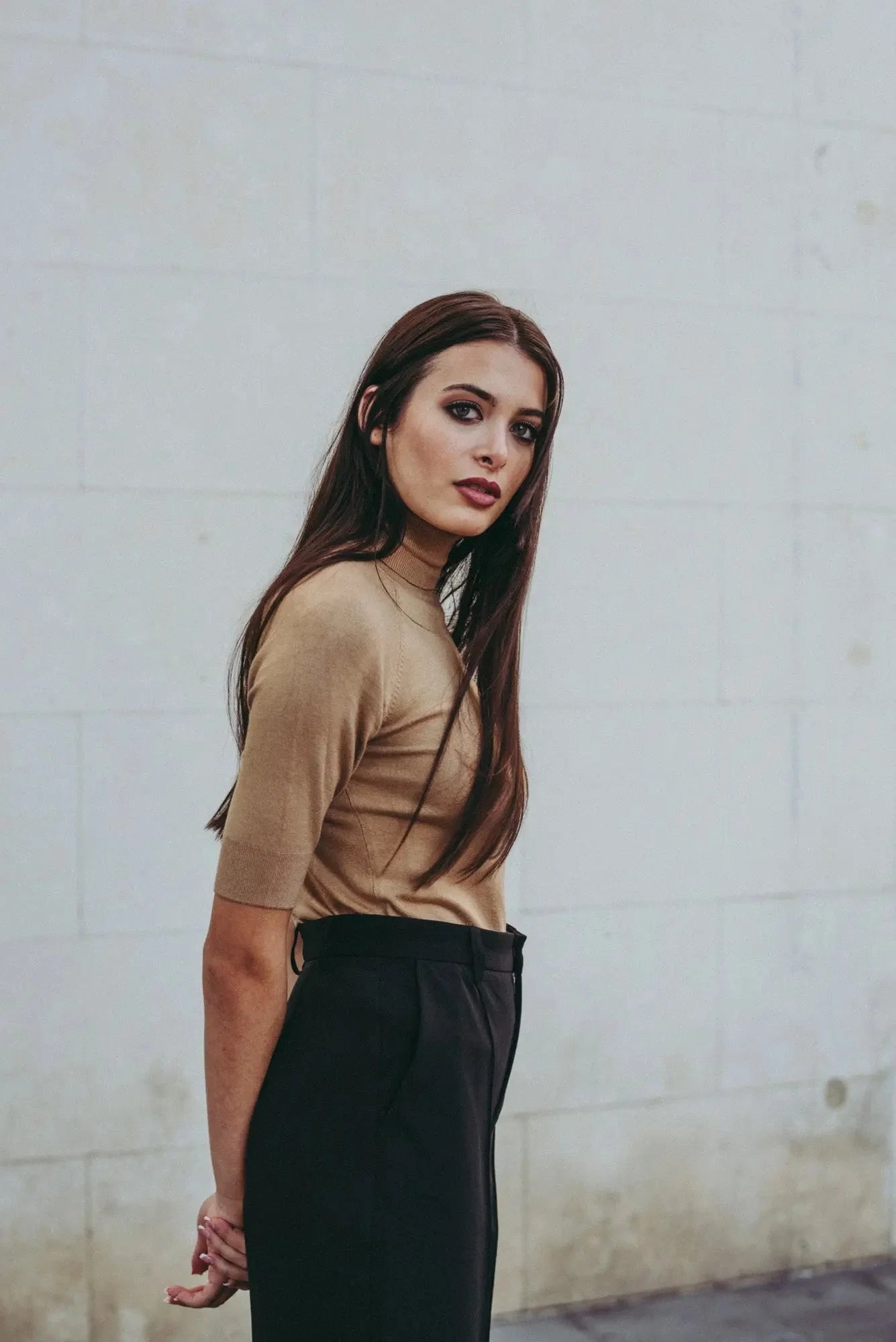 Femme portant un pull tricoté beige à col roulé et pantalon noir élégant
