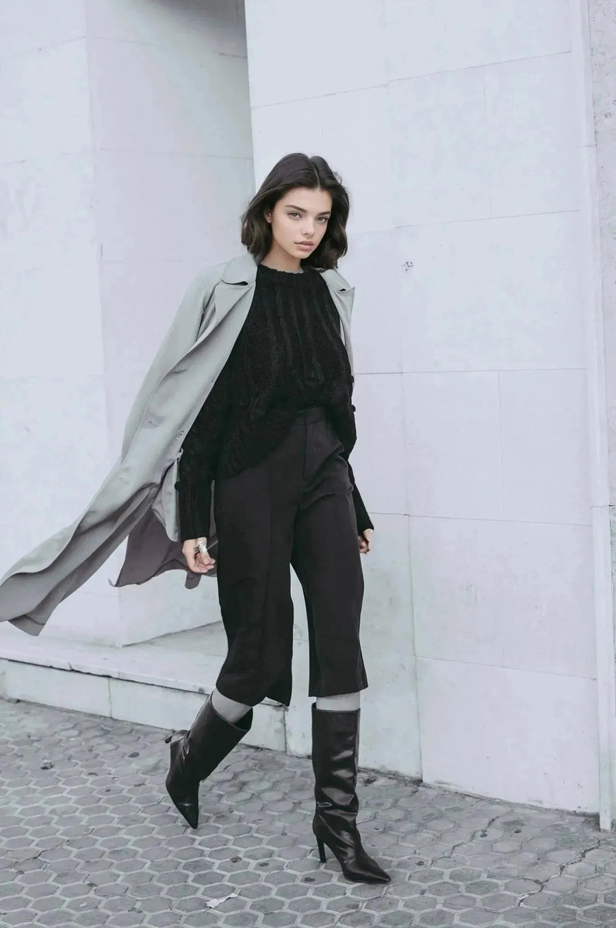 Femme habillée d'un pull laine femme noir à torsades, marchant avec assurance en manteau élégant, idéal pour le style polyvalent.